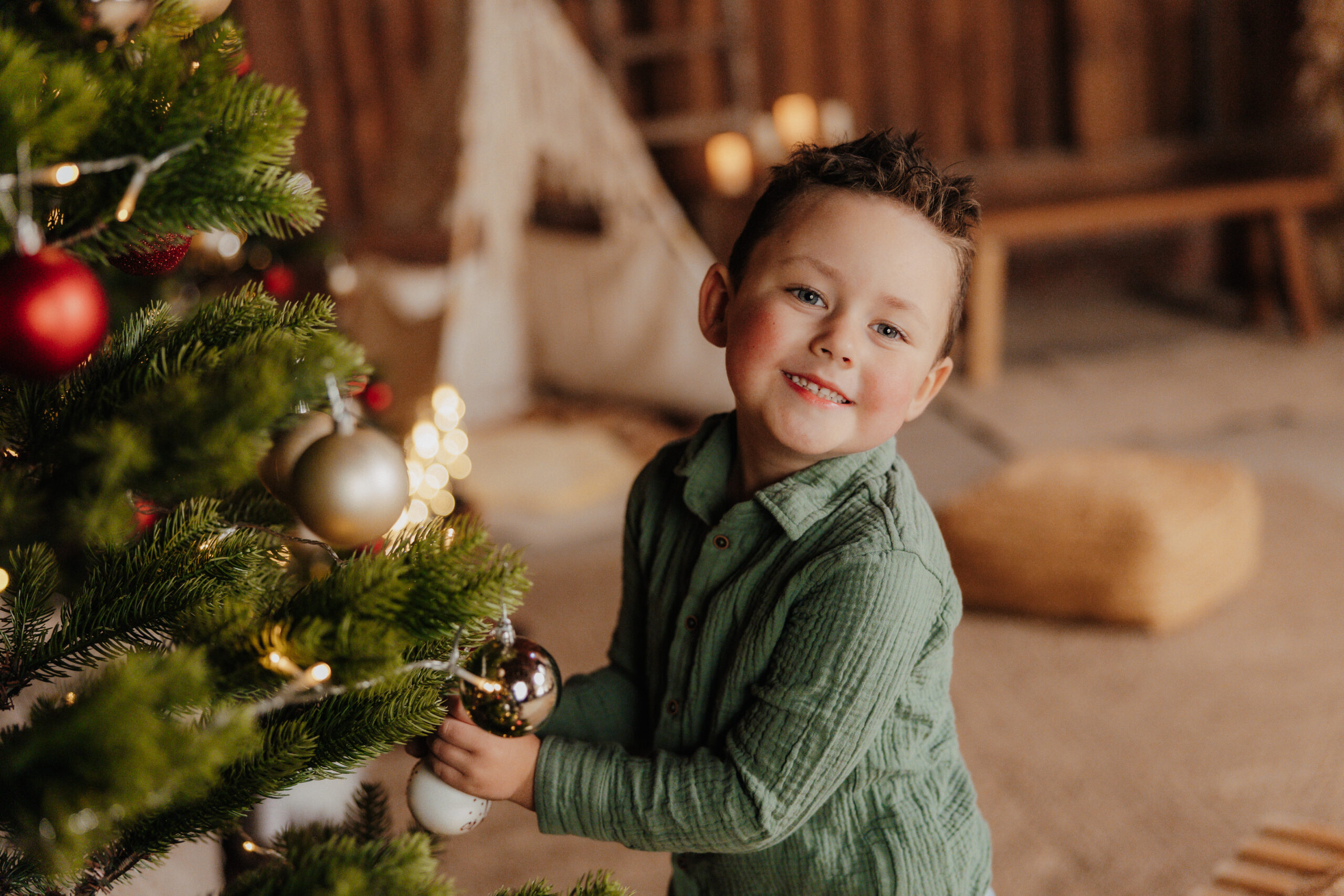 Kind mit einer Weihnachtskugel neben dem geschmückten Tannenbaum