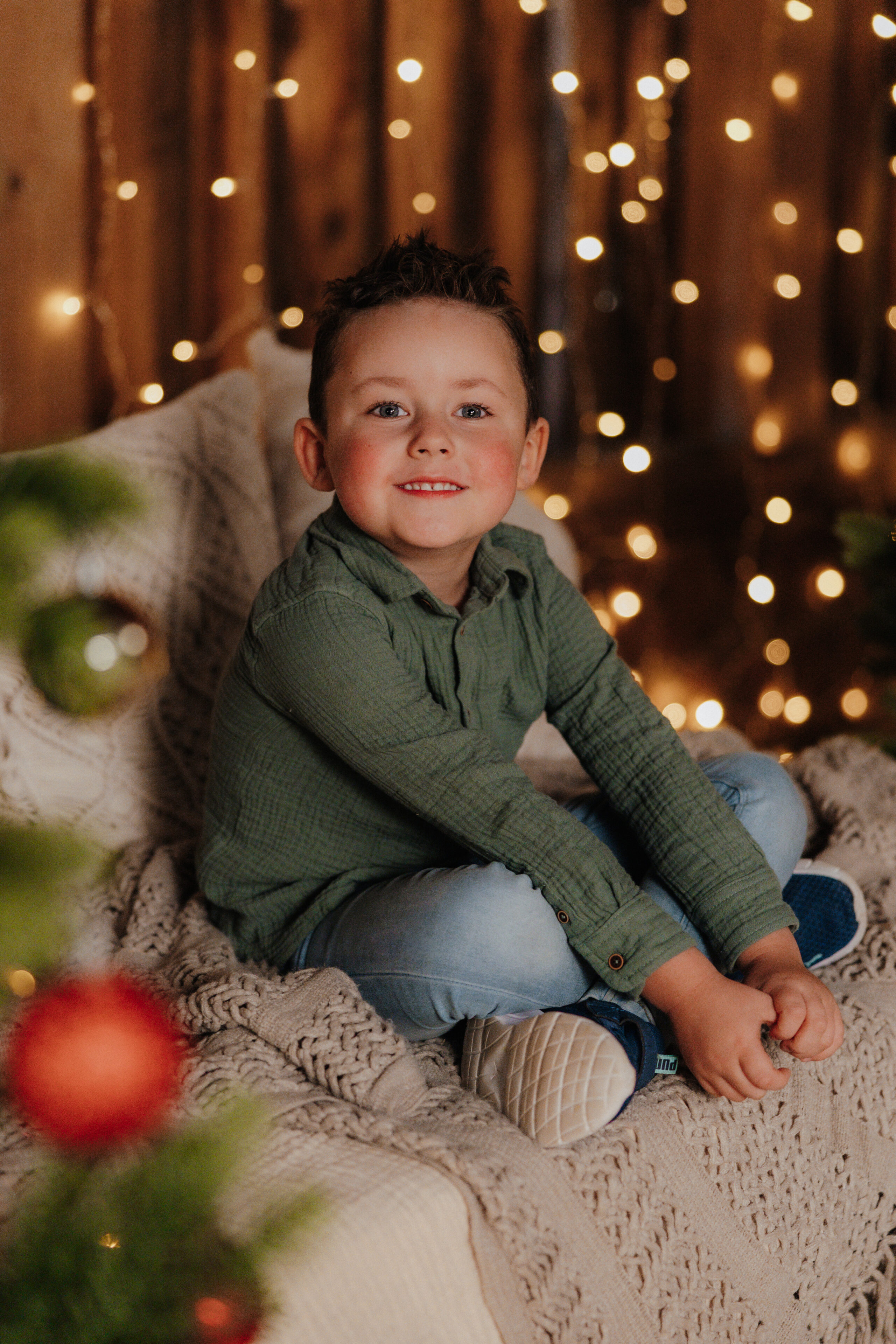 Lachendes Kind auf dem Sofa vor warmen Weihnachtslichtern